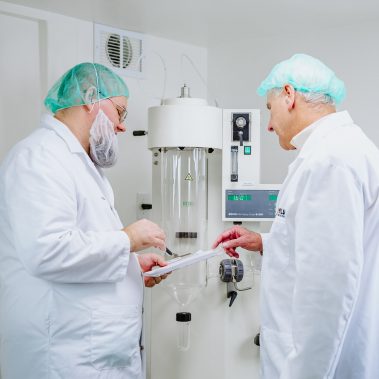 Scientists reviewing data next to a compact spray dryer system, demonstrating the precise operation of small spray dryers for research and development.