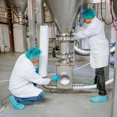 Technicians operating an industrial spray dryer, demonstrating the hands-on quality control process for the spray drying systems provided by http://pulsedry.com/.