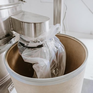 A sealed plastic bag containing product is being discharged into a large collection drum, a critical step in the process of industrial spray drying equipment and powder dryers offered by http://pulsedry.com/.