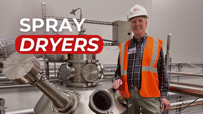 A smiling man in a hard hat and safety vest stands next to a large stainless steel industrial spray dryer, with overlaid text 'SPRAY DRYERS'