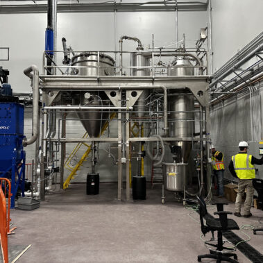 A complete P-50 industrial spray dryer system from Pulse.com, with technicians managing the control panel, demonstrating a full-scale industrial drying solution in action