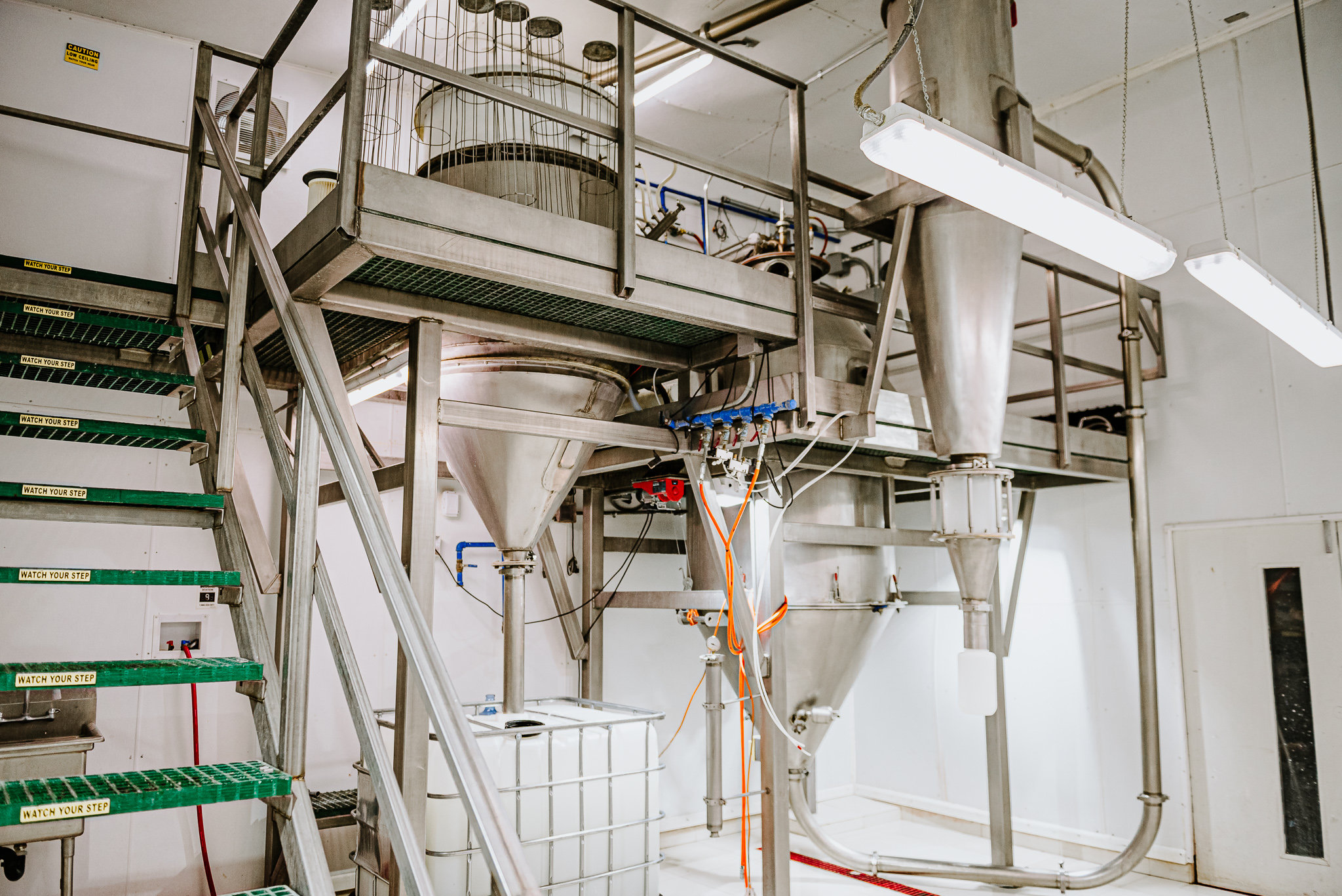 A wide-angle view of a multi-level industrial drying facility featuring Pulse Combustion Systems' stainless steel spray drying towers, interconnected piping, and a raised metal catwalk.