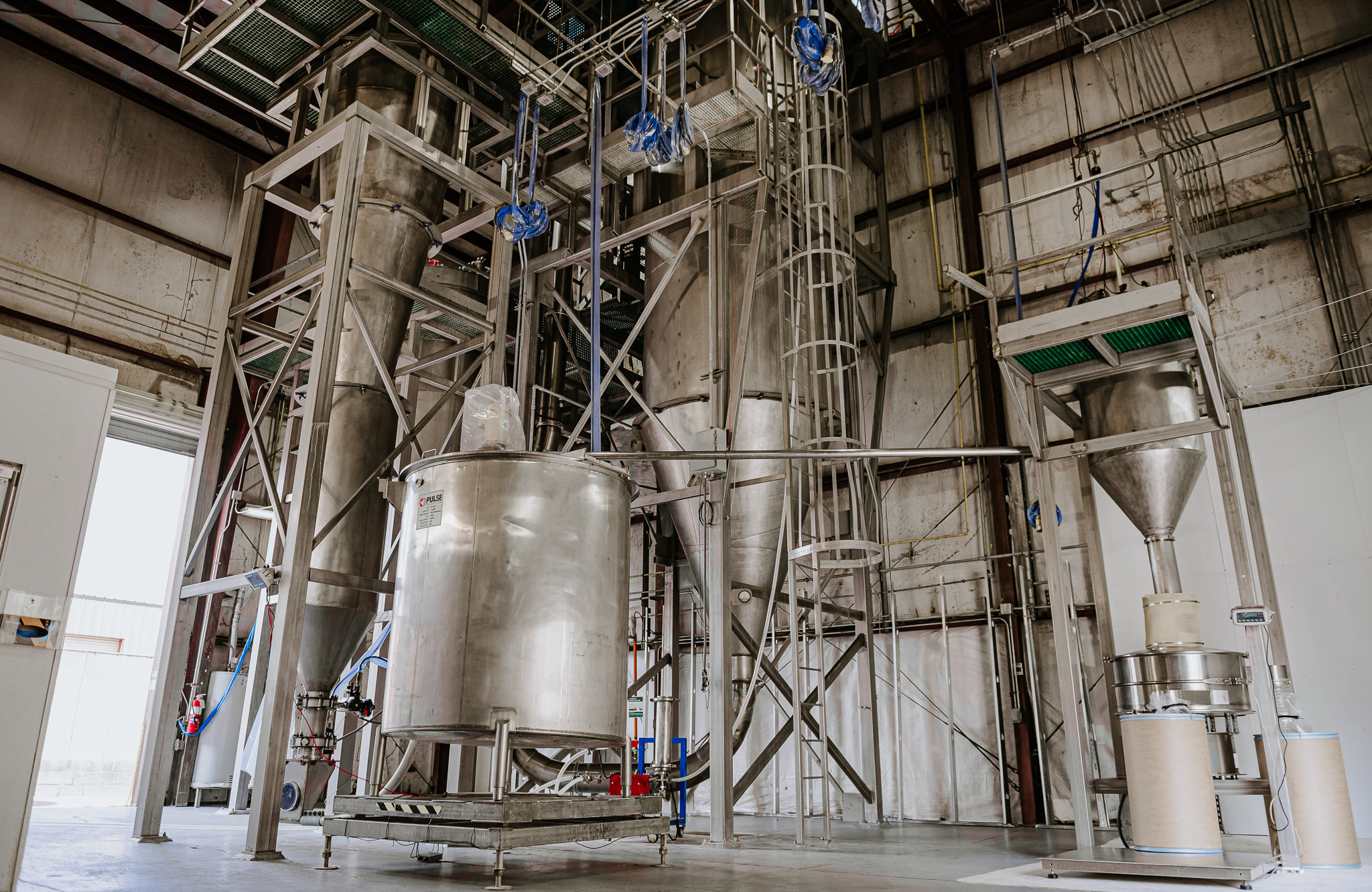 A low-angle view of a multi-level industrial drying facility featuring Pulse Combustion Systems' tall stainless steel spray drying towers and professional manufacturing infrastructure.